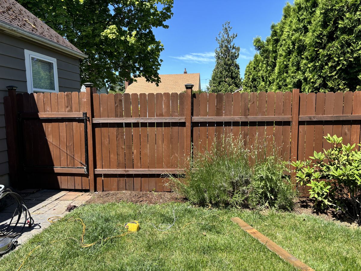 Stained wood privacy fence with a matching gate along a backyard garden bed